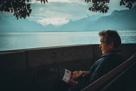 Elderly man sitting alone with a book looking at a water scenery.