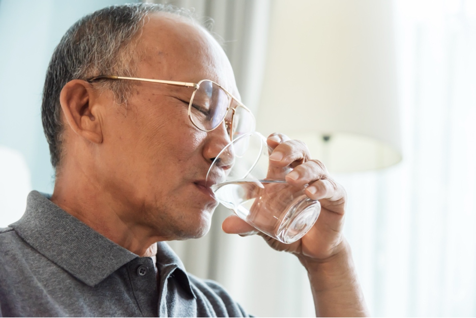 Elderly Asian man drinking water from a glass.